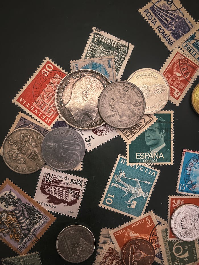 A flatlay of antique coins and vintage stamps from various countries on a dark background.